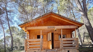 A wooden cabin with a stone foundation, a wooden porch, and a sign reading 'LA CAPELLANIA'.