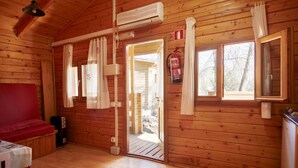 A wooden cabin interior with a bed, a fire extinguisher, and a door leading outside.