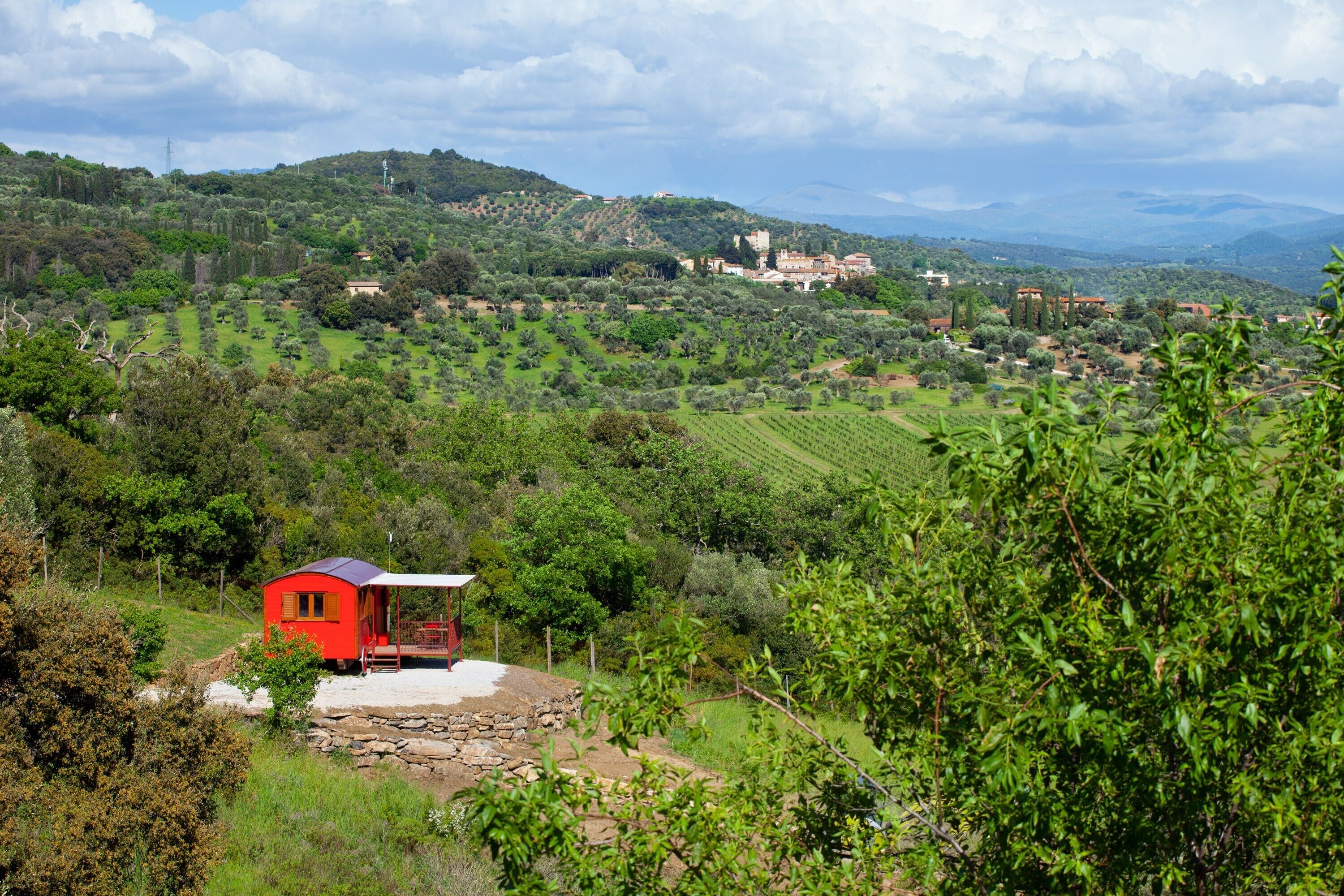 A red building with a white roof, surrounded by lush greenery and hills.