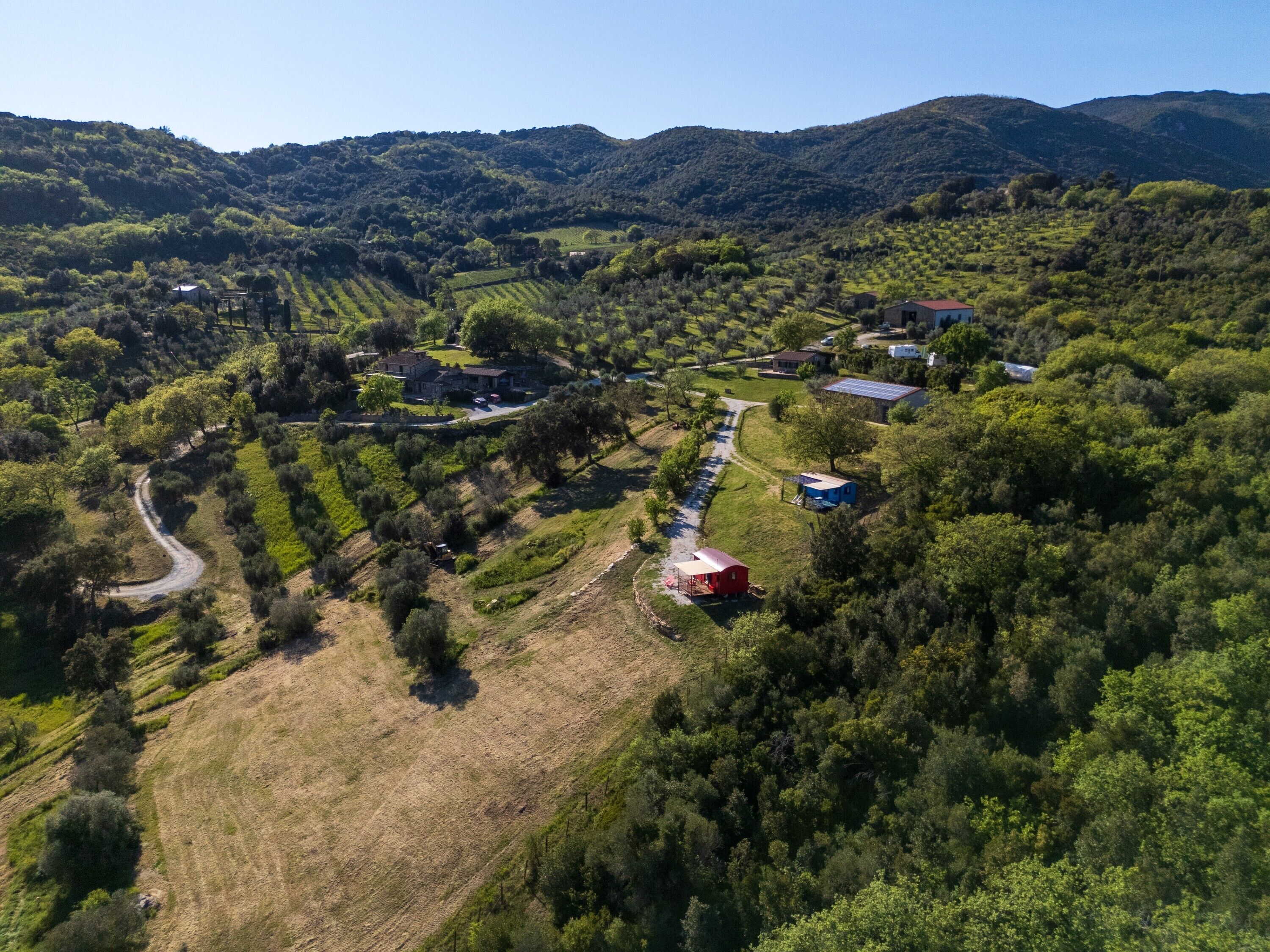 An aerial view of a rural property with a winding road, multiple buildings, and surrounding lush greenery.