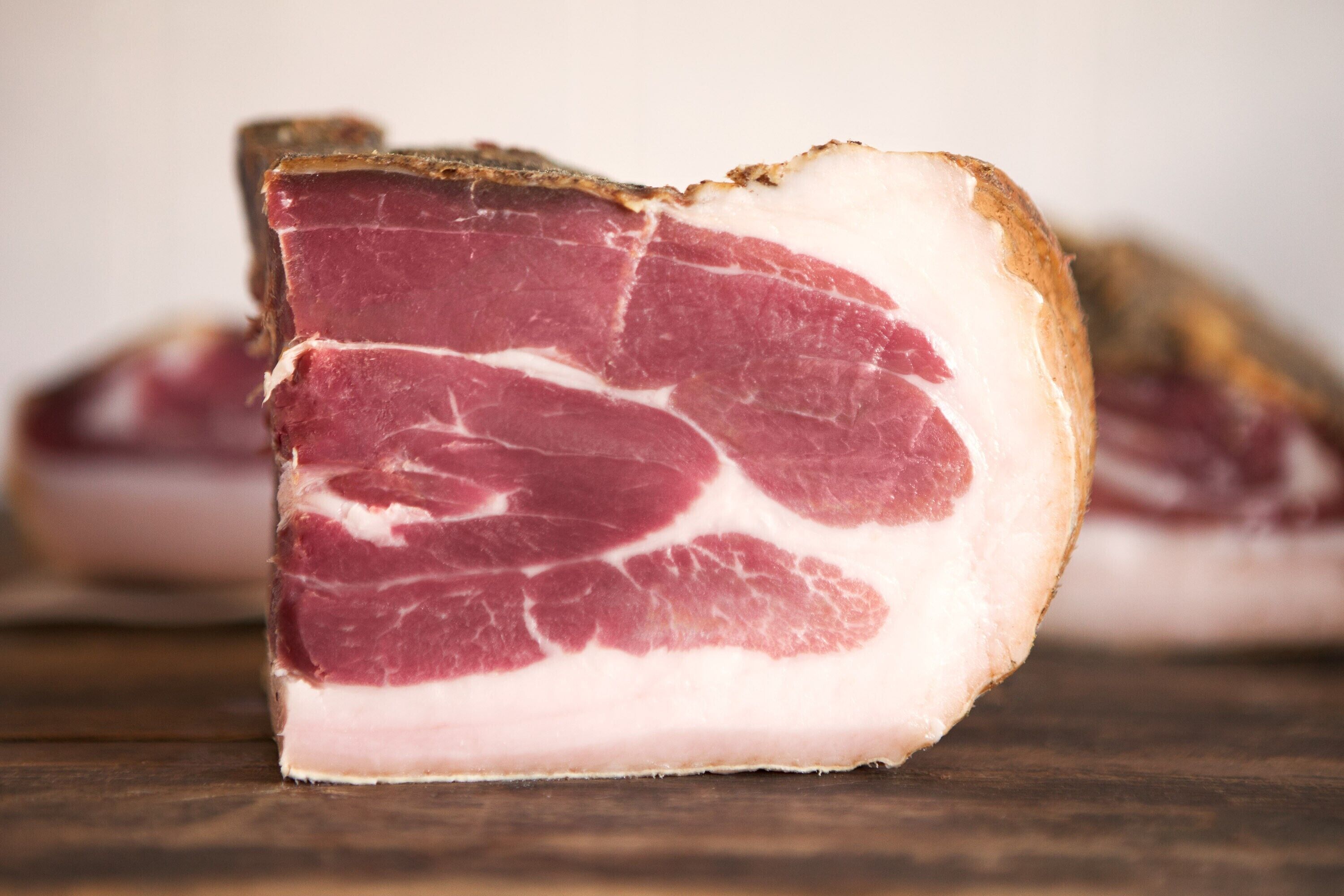 Un trozo de carne curada con capas visibles de grasa y una costra.