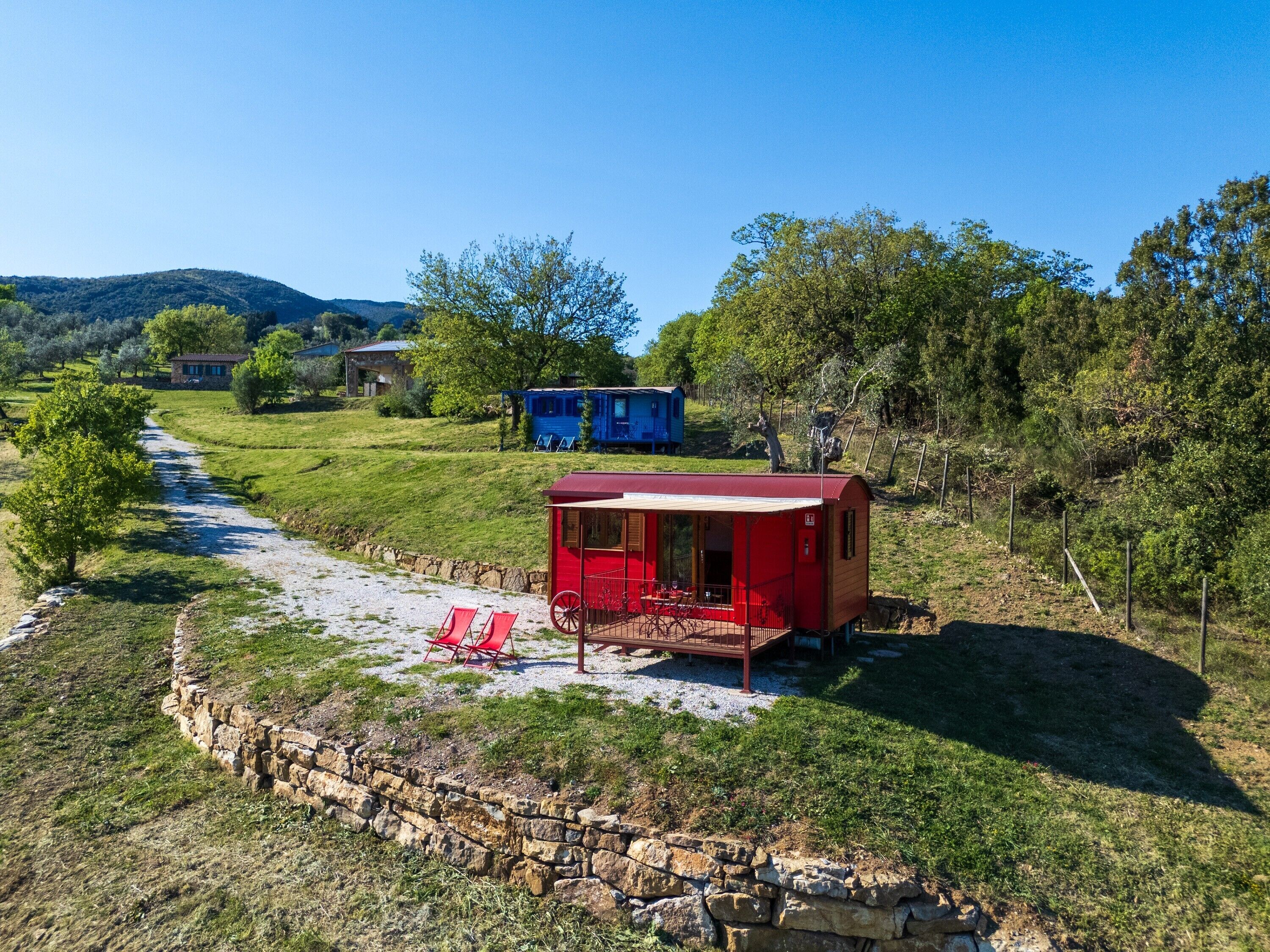 A red cabin with a porch, a gravel path, and a stone wall.