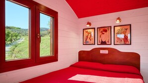 Een slaapkamer met een houten hoofdbord, een rode sprei en drie ingelijste kunstwerken aan de muur.