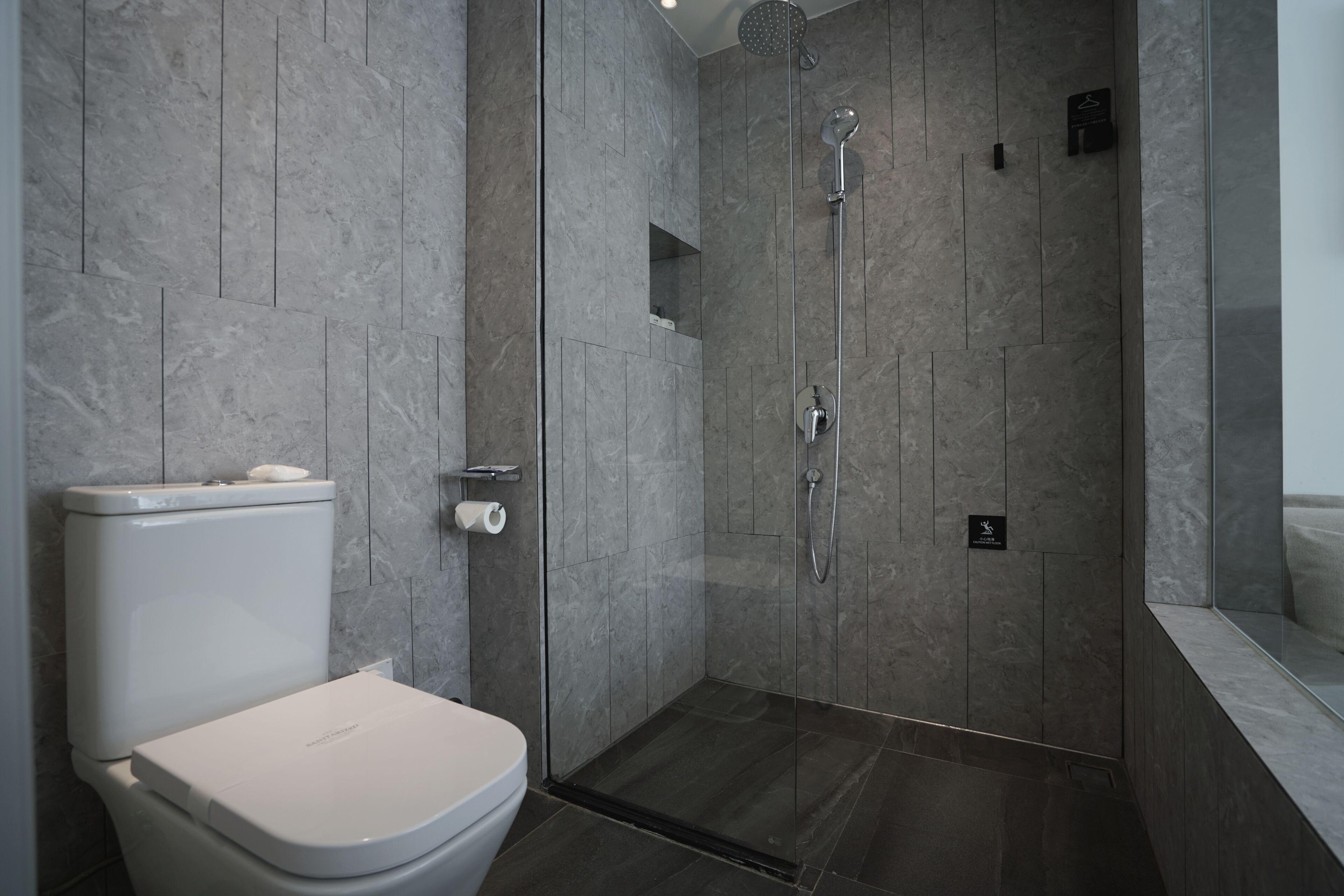 A modern bathroom with a toilet, a glass-enclosed shower, and a marble wall.