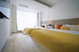 Habitación de hotel con dos camas, un ventanal con cortinas, una mesita de noche con lámpara y un cabecero con iluminación.