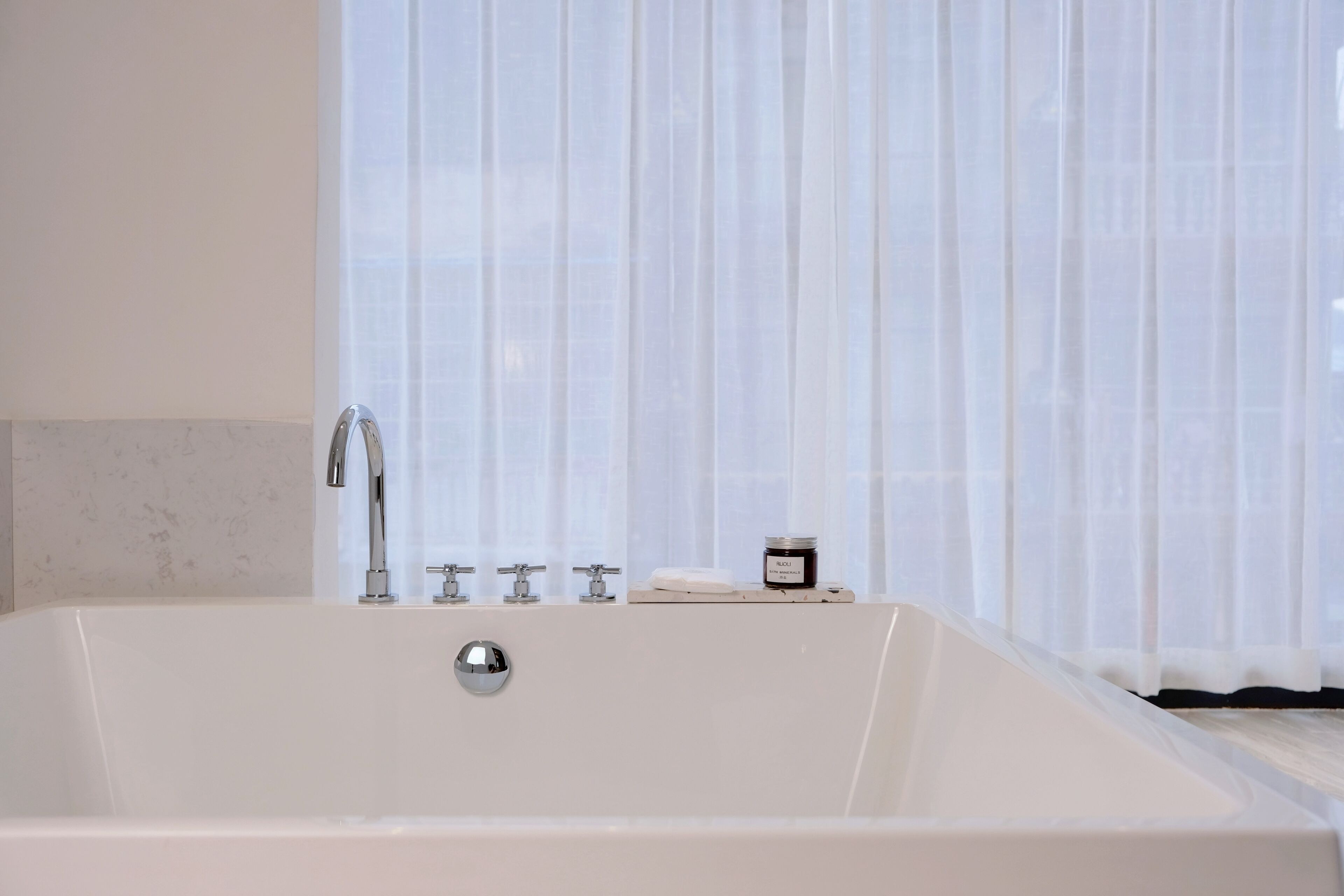 Una bañera blanca con grifo cromado y un pequeño estante con un tarro y una pastilla de jabón.