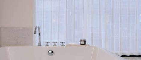 A white bathtub with a chrome faucet and a small shelf with a jar and a soap bar.