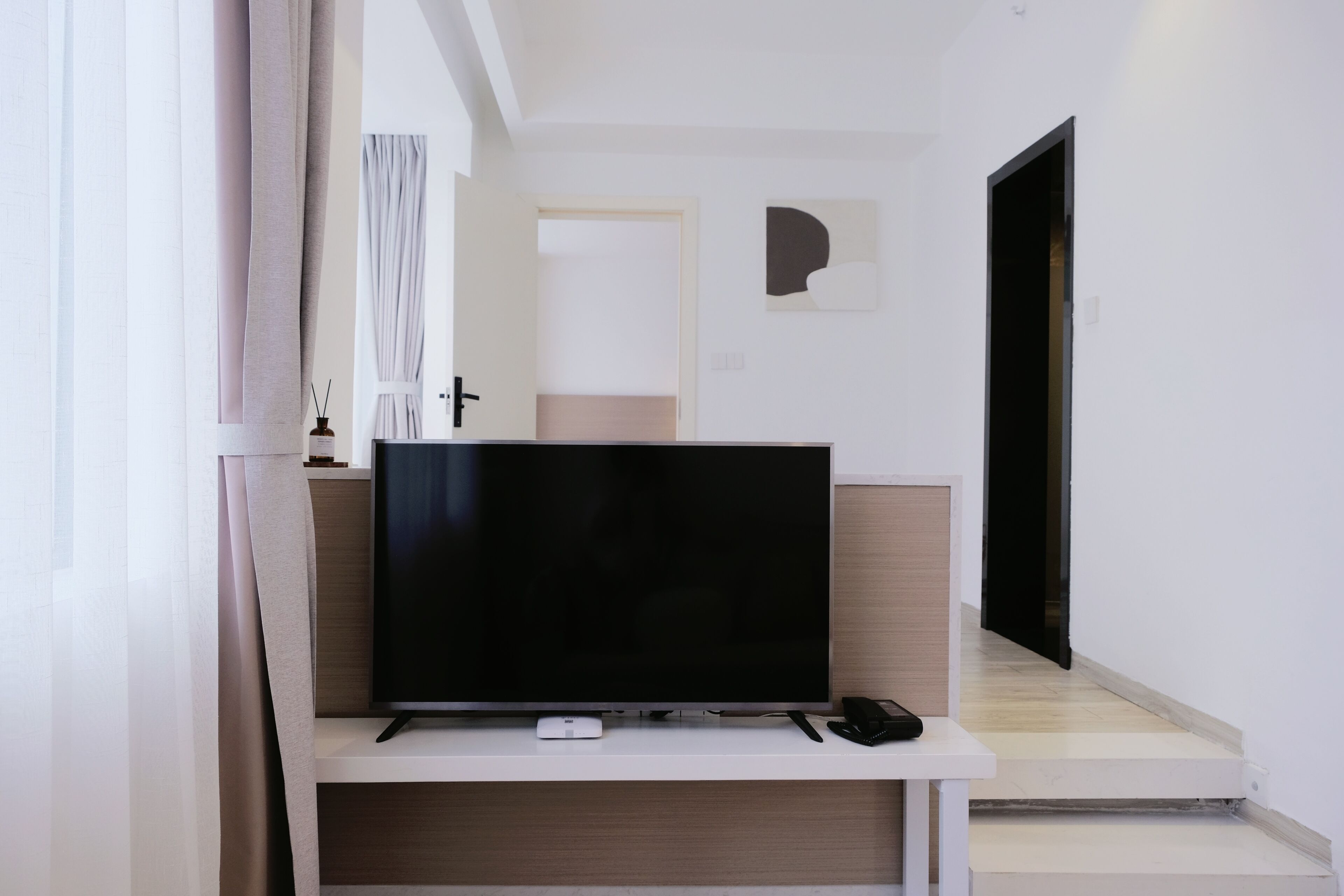 A modern living room with a flat-screen TV on a white stand, a remote control, and a small white device on the stand.