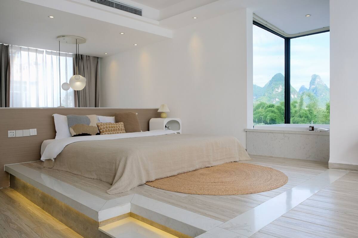 A modern bedroom with a large bed, a view of mountains, and a large window.