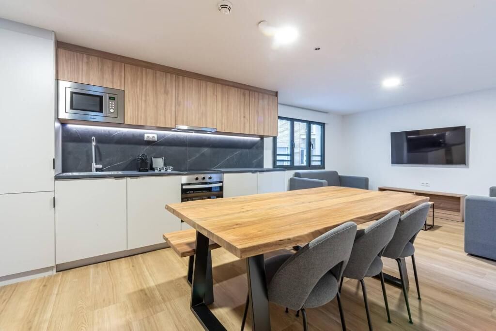 Una cucina moderna con un tavolo e sedie in legno, un forno a microonde e una televisione.
