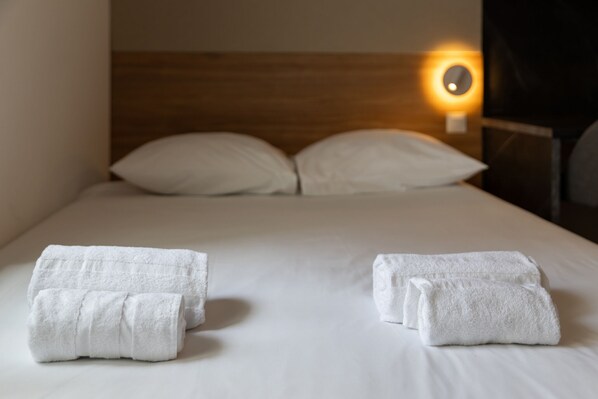 Een net opgemaakt bed met witte lakens en twee opgerolde handdoeken.