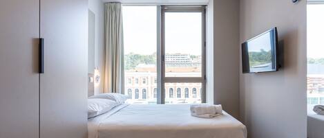 Une chambre d’hôtel avec un grand lit, un téléviseur fixé au mur et une fenêtre donnant sur la ville.