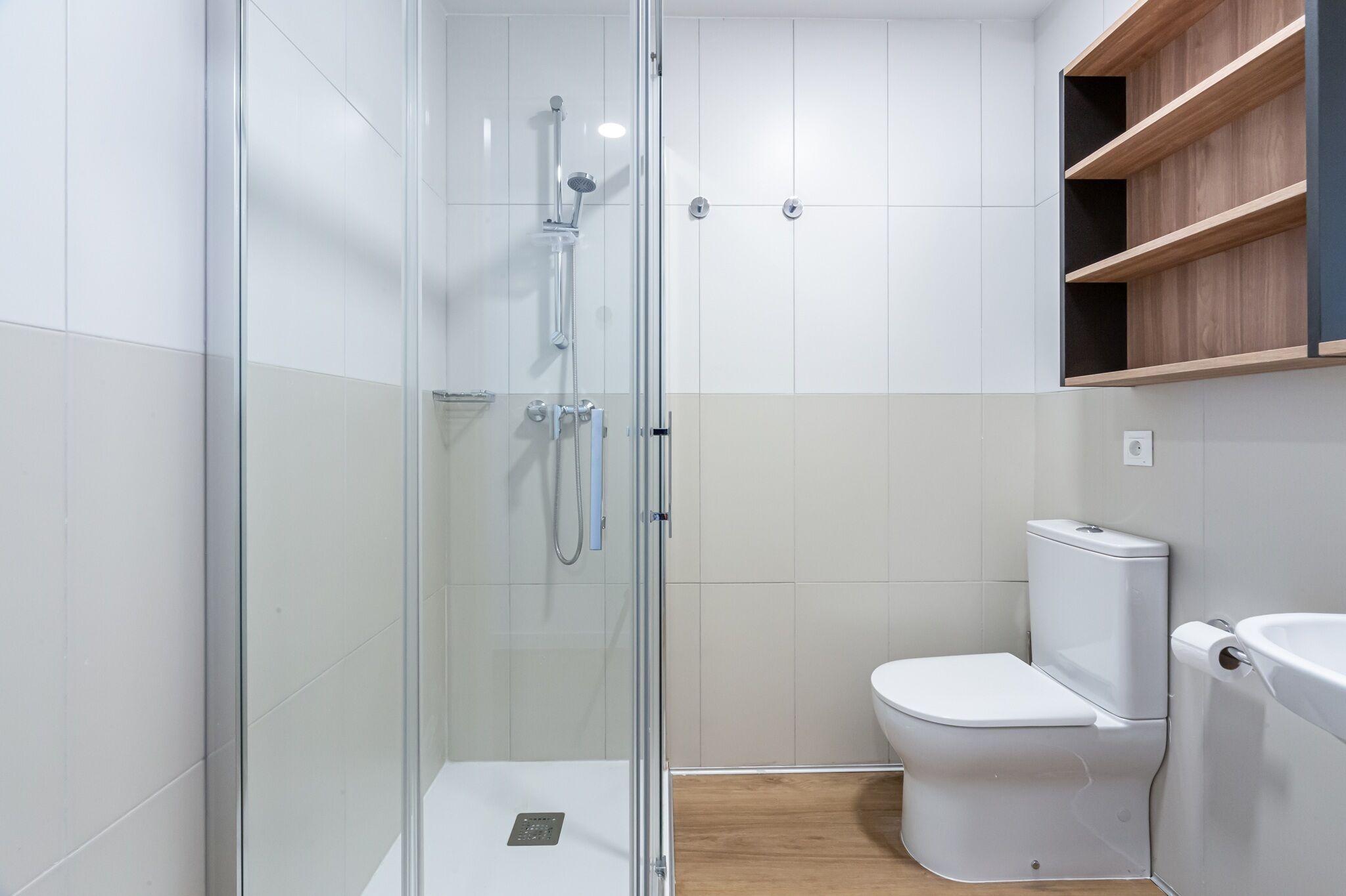 Un baño moderno con cabina de ducha de vidrio, inodoro blanco y estante de madera.