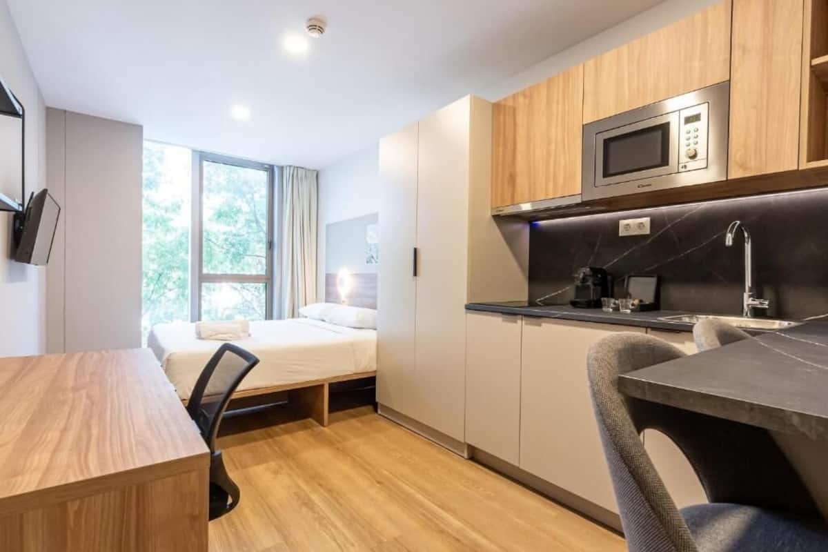 Une chambre d’hôtel compacte comprenant un coin cuisine, un lit près d’une fenêtre et un bureau.