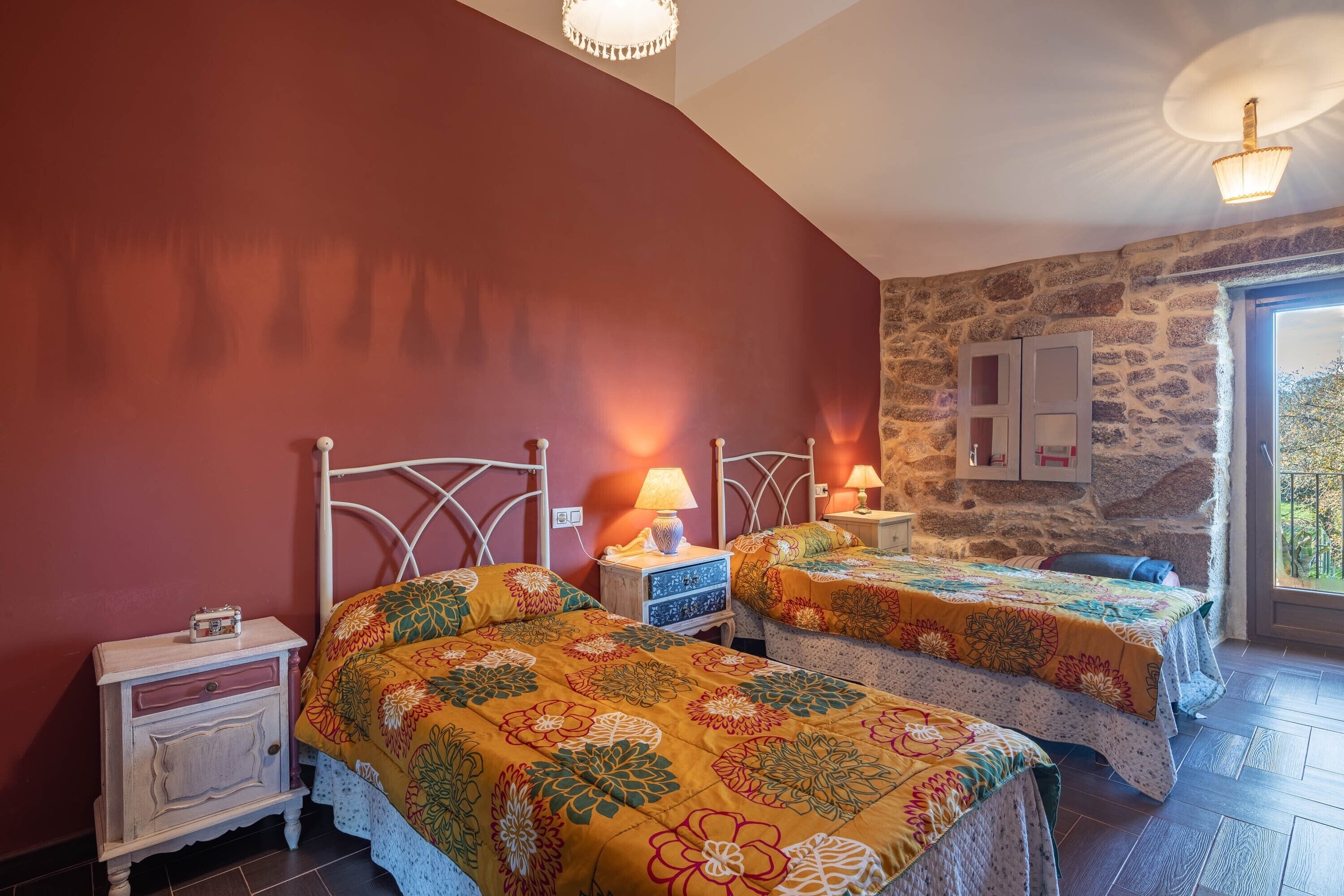 Une chambre avec deux lits, un mur en pierre, une fenêtre et une table de chevet avec une lampe.