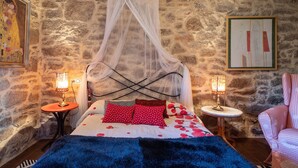 A bedroom with a stone wall, a bed with a canopy, two bedside tables with lamps, and a chair. - Rural House 'Chan Da Ra' with Mountain Views, Private Pool and Private Terrace (A Lama)