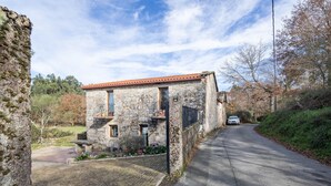 A stone building with a red-tiled roof, a paved driveway, and a car parked on the road. - Rural House 'Chan Da Ra' with Mountain Views, Private Pool and Private Terrace (A Lama)