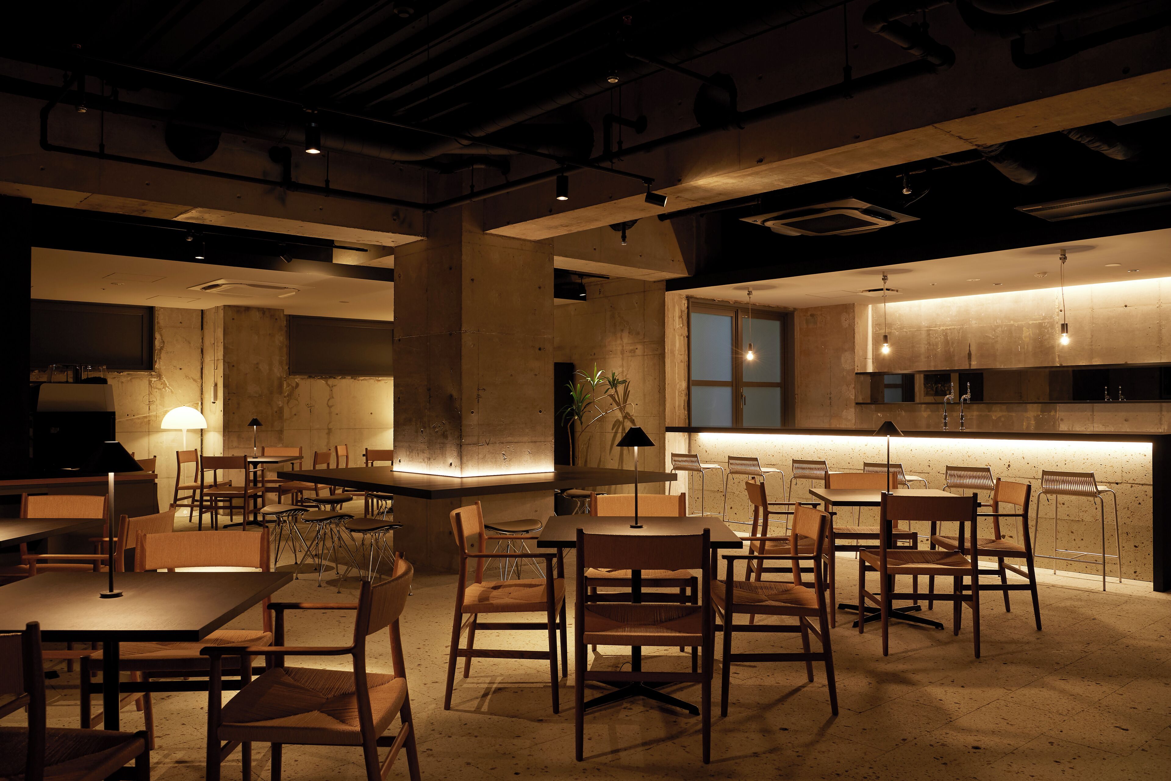 A spacious dining area with multiple tables and chairs, a central island with seating, and a kitchen area in the background.