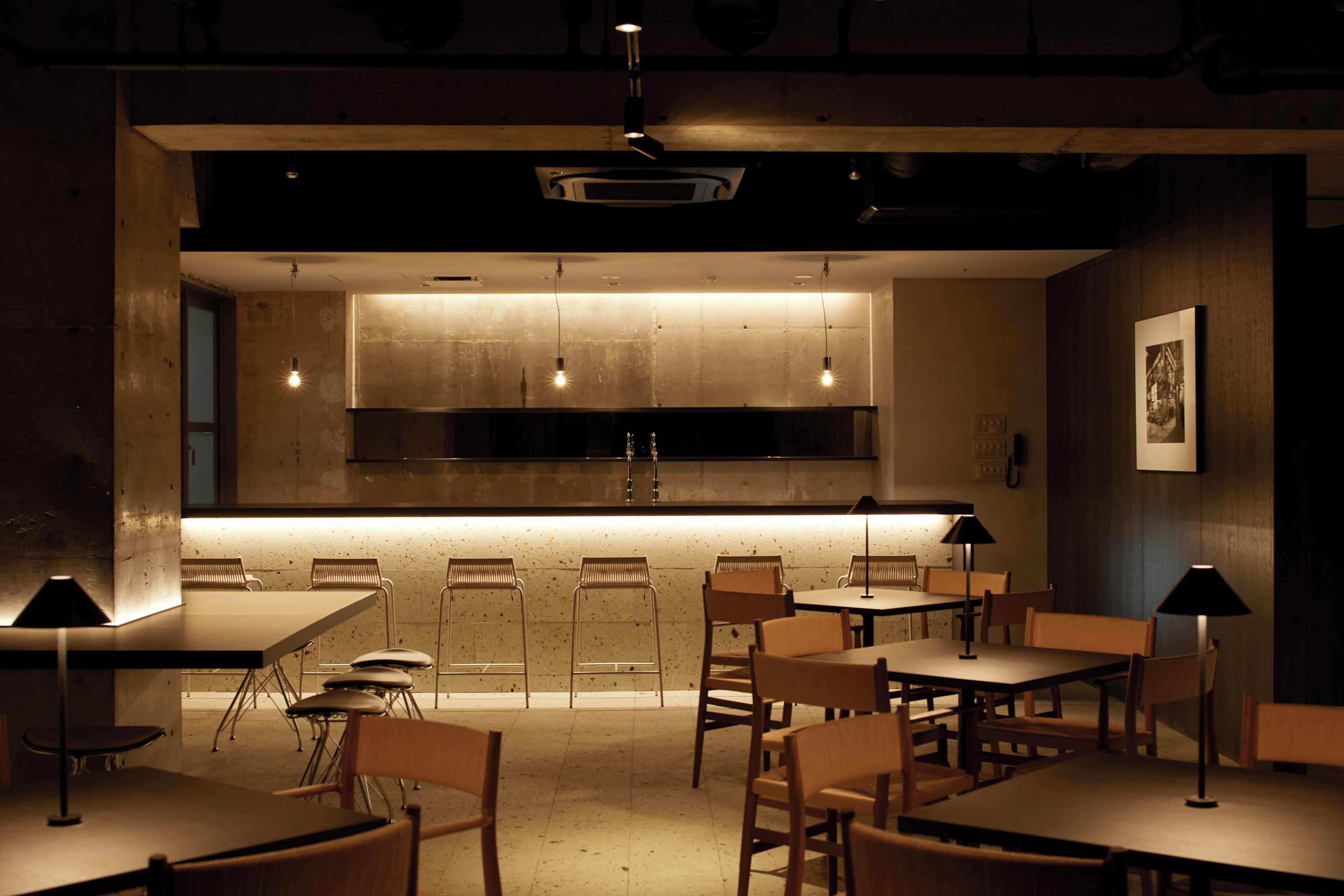 A modern restaurant with a central kitchen, wooden tables and chairs, and pendant lighting.