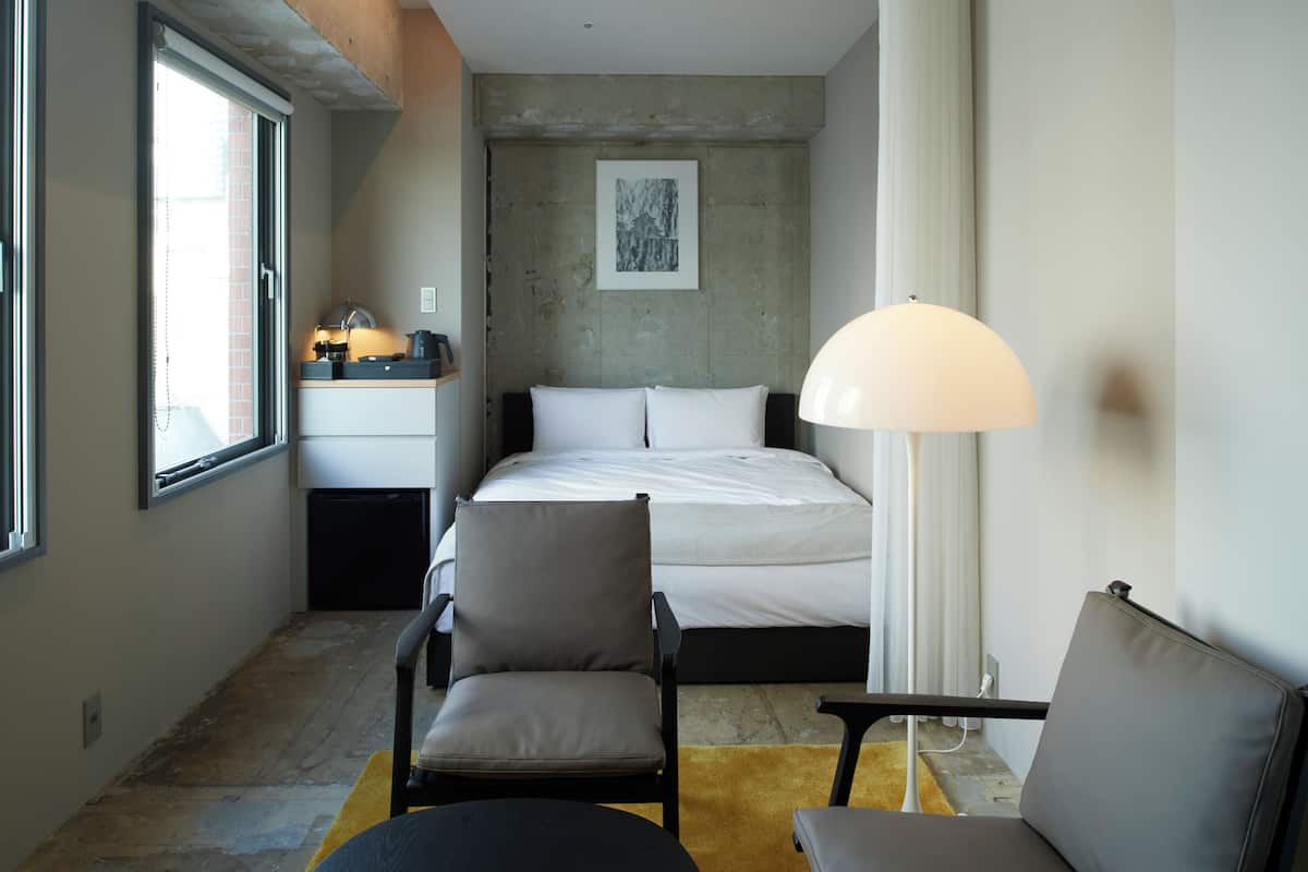 A bedroom with a bed, two chairs, a desk, and a lamp.