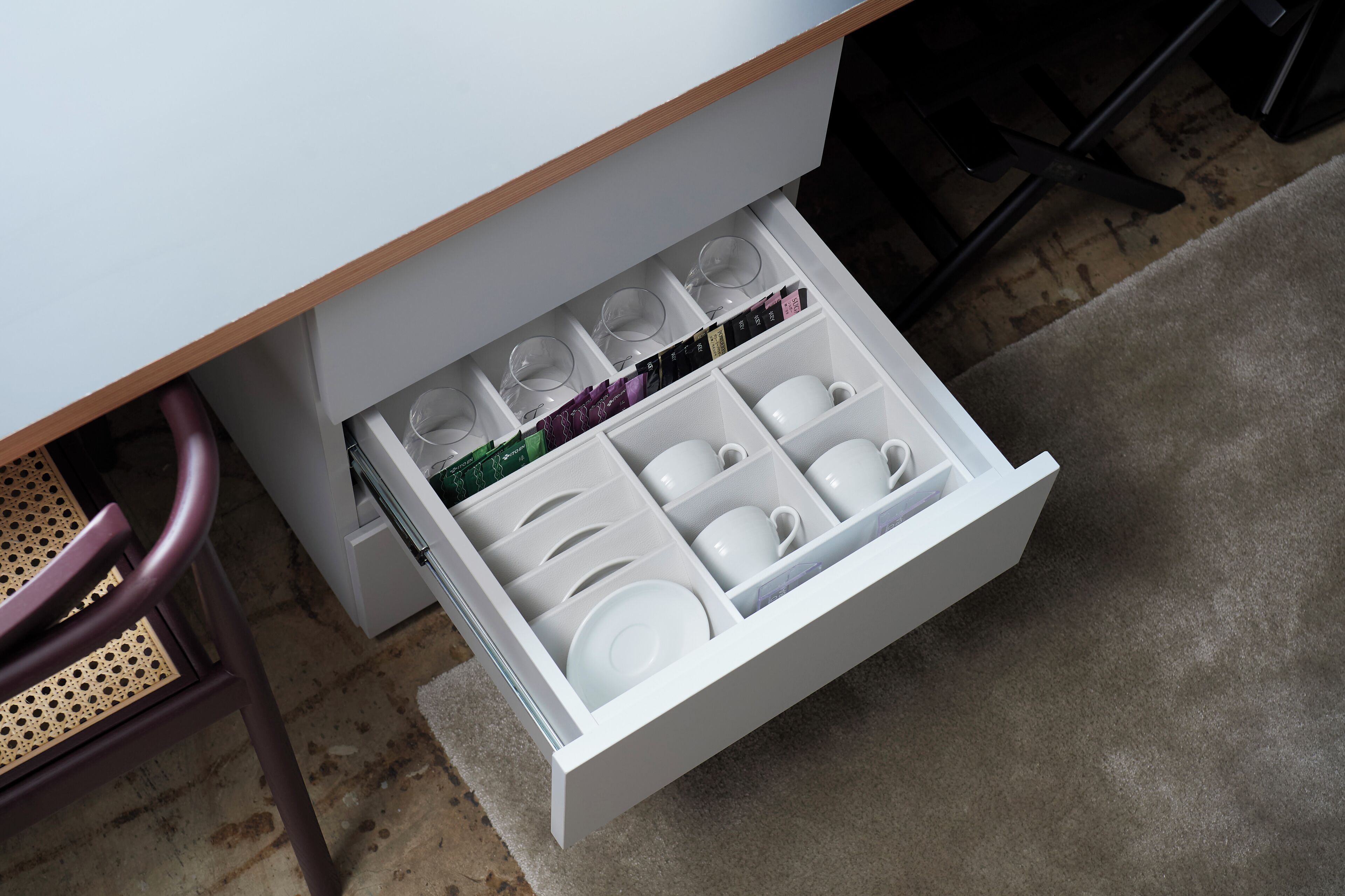 Un tiroir blanc situé sous une table, avec des compartiments pour les tasses, les assiettes et les verres.