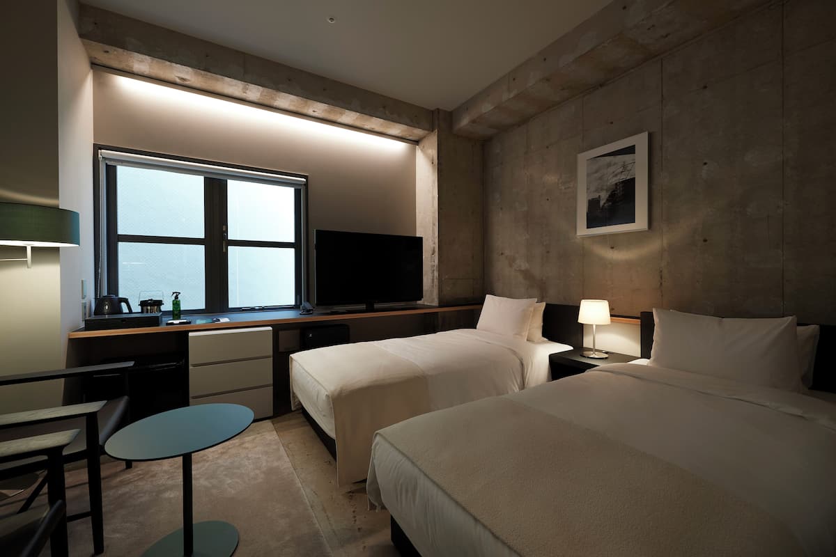 A hotel room with two beds, a desk with a computer, a television, a window with a view, and a small table.