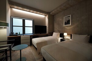 A hotel room with two beds, a desk with a computer, a television, a window with a view, and a small table.