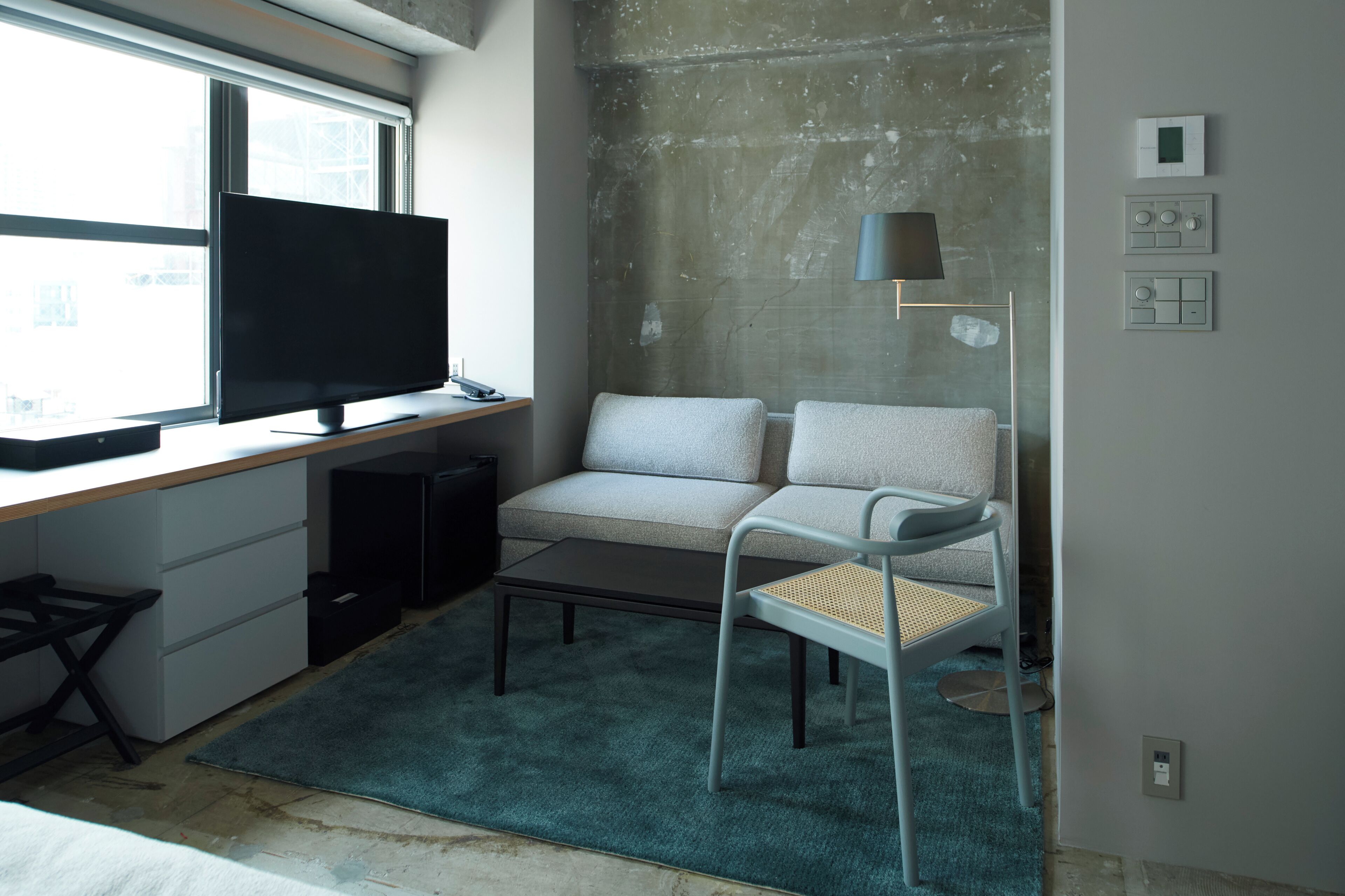 Una habitación moderna con un ventanal grande, un televisor de pantalla plana, un sofá, una silla, una mesita de café y una lámpara.
