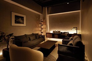 A modern living room with a sofa, coffee table, and chairs. There is a framed picture on the wall and a lamp on a side table. - TONES OSAKA (Osaka)