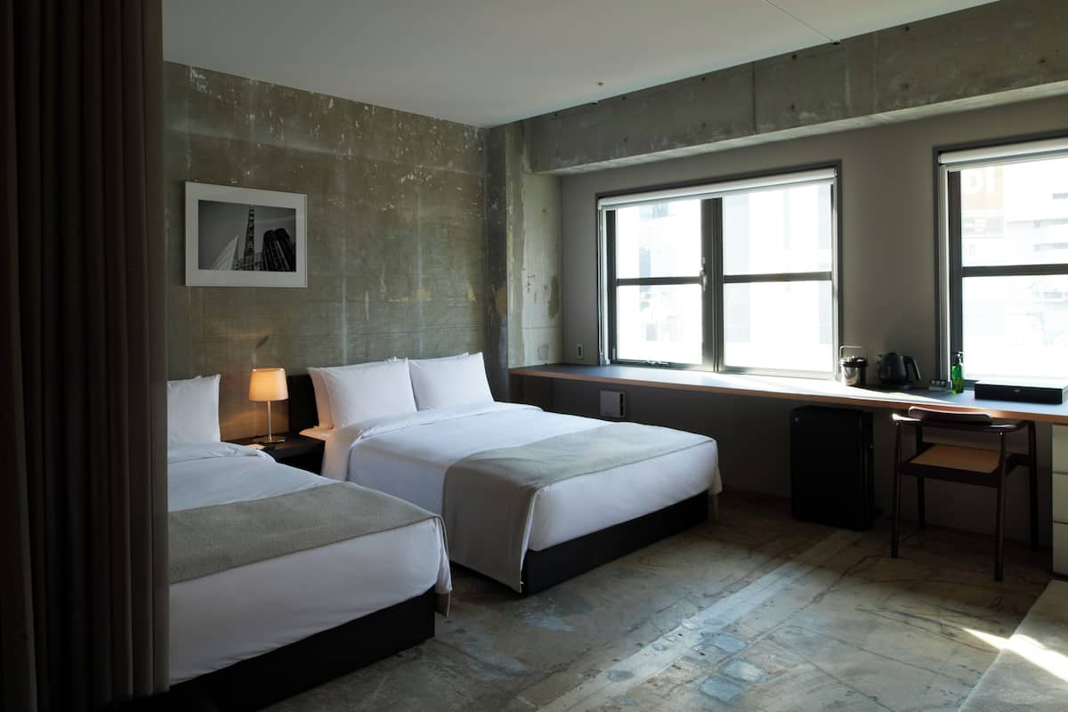 A hotel room with two beds, a desk, a chair, a window, and a picture on the wall.