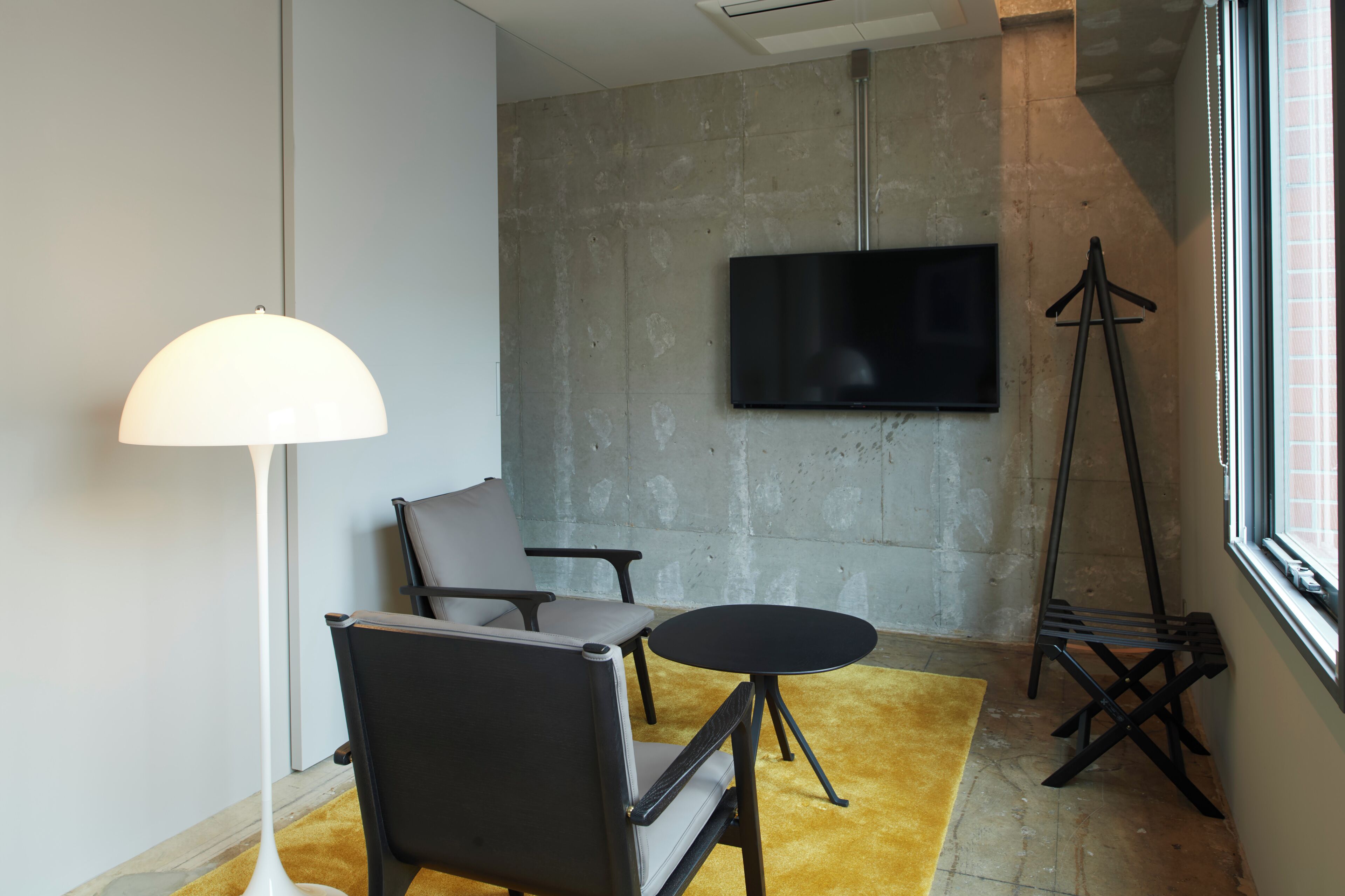 A modern room with a sofa, a small table, a floor lamp, a TV mounted on the wall, and a tripod stand.