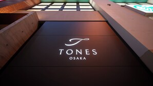 Ein modernes Gebäude mit einem auffälligen Schild, das im Erdgeschoss „TONES OSAKA“ zeigt.