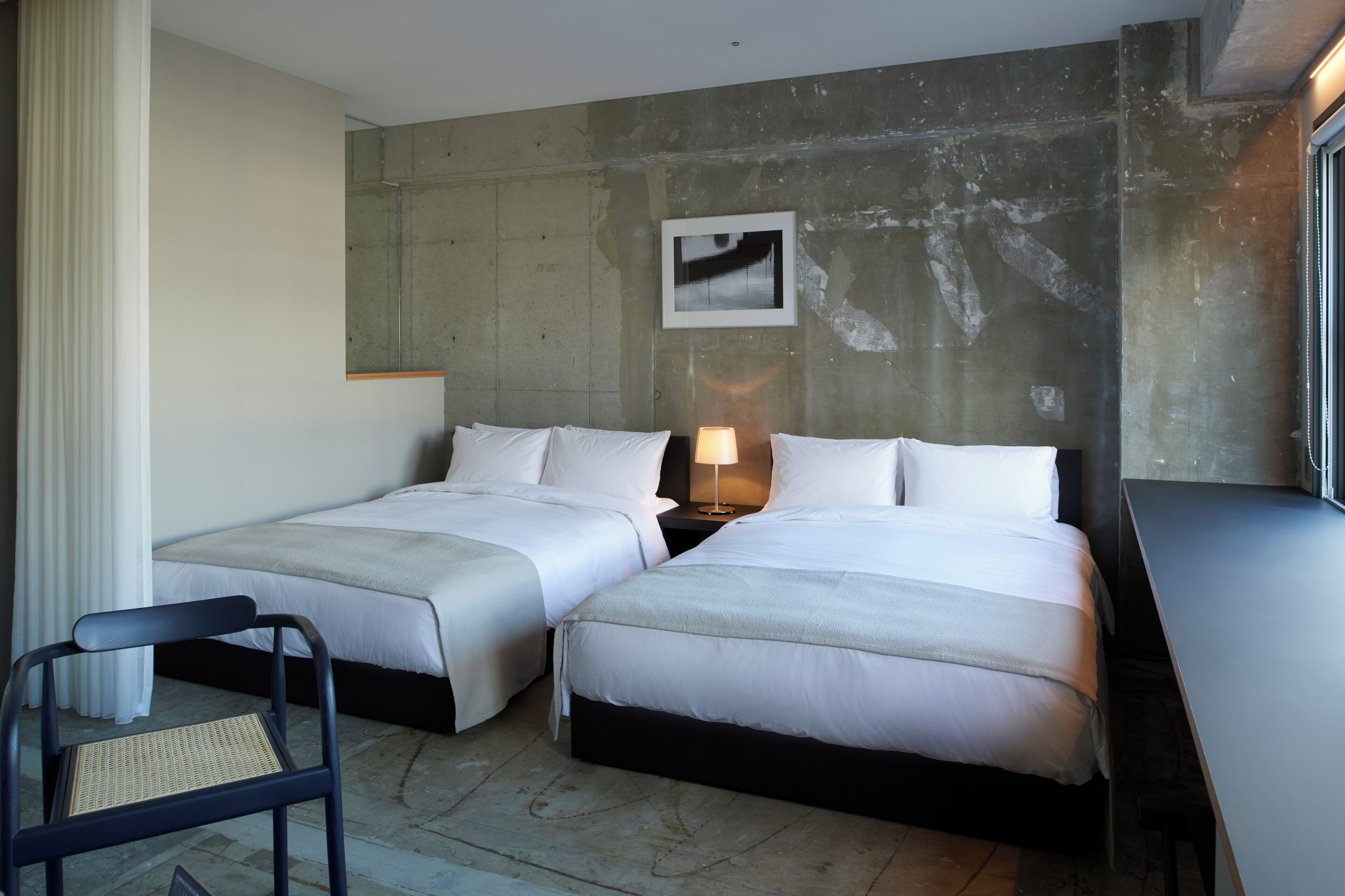 Habitación de hotel con dos camas, un escritorio, una silla, una lámpara y un cuadro en la pared.