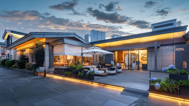 A modern hotel with outdoor seating, a well-lit entrance, and a view of the city skyline. - Papman Hotel (Kunming)