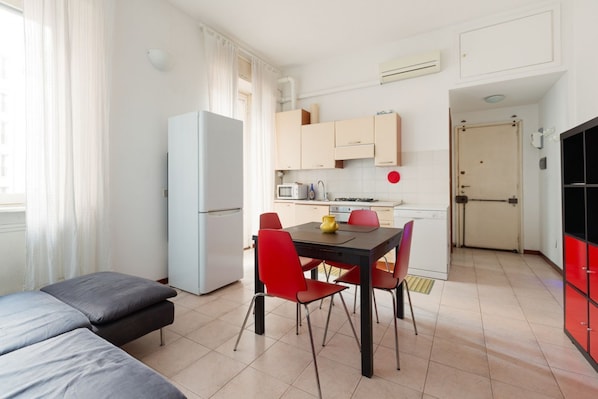 A compact room with a bed, a dining table with chairs, a kitchenette, and a door leading to another room.