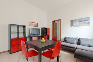 A modern living room with a dining area, red and grey furniture, a television, and a painting on the wall.