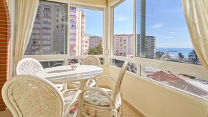 Un balcon avec une table et des chaises, un pot de fleurs et une vue sur les bâtiments et la mer.