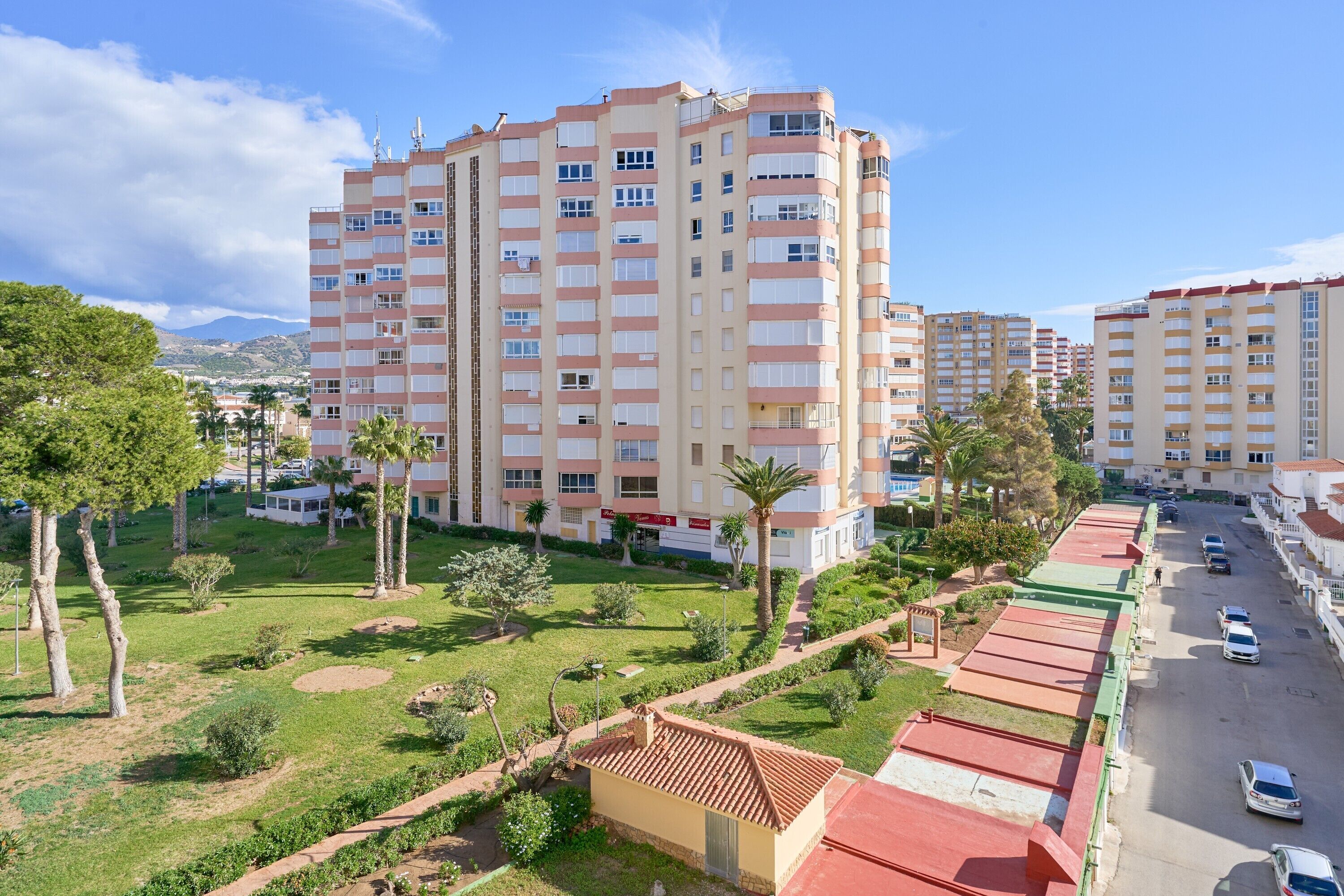 Un edificio residencial de varios pisos con un patio central, rodeado de vegetación y palmeras.