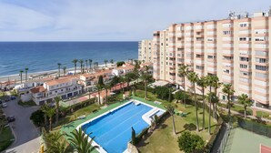 Un immeuble résidentiel doté d’une piscine, de palmiers et offrant une vue sur la mer.