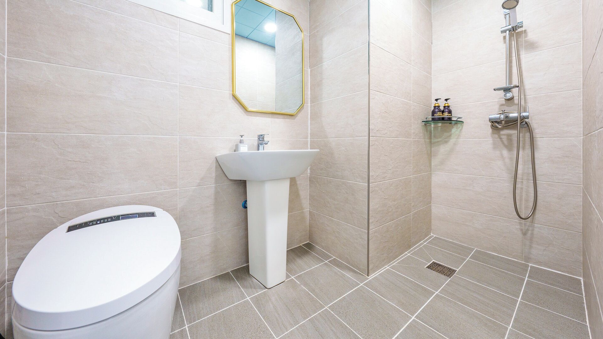 A bathroom with a toilet, sink, mirror, shower, and a glass shelf with toiletries.