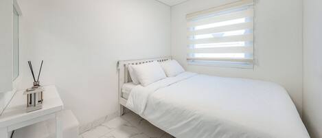 A bedroom with a bed, a bedside table, and a window with blinds.