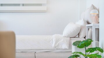 Un dormitorio minimalista con cama, almohadas, una mesita de noche con lámpara y una planta.