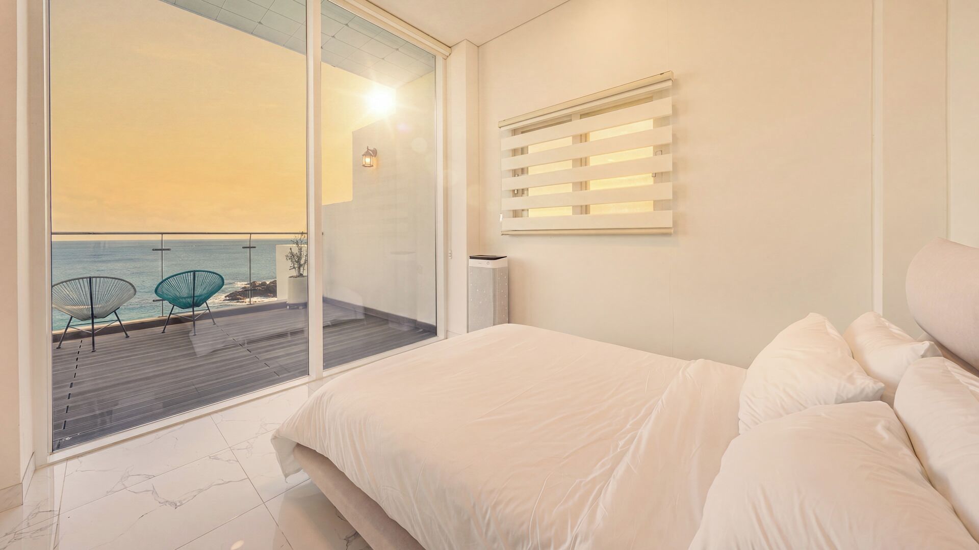 A bedroom with a large bed, a view of the sea, and a balcony with chairs.