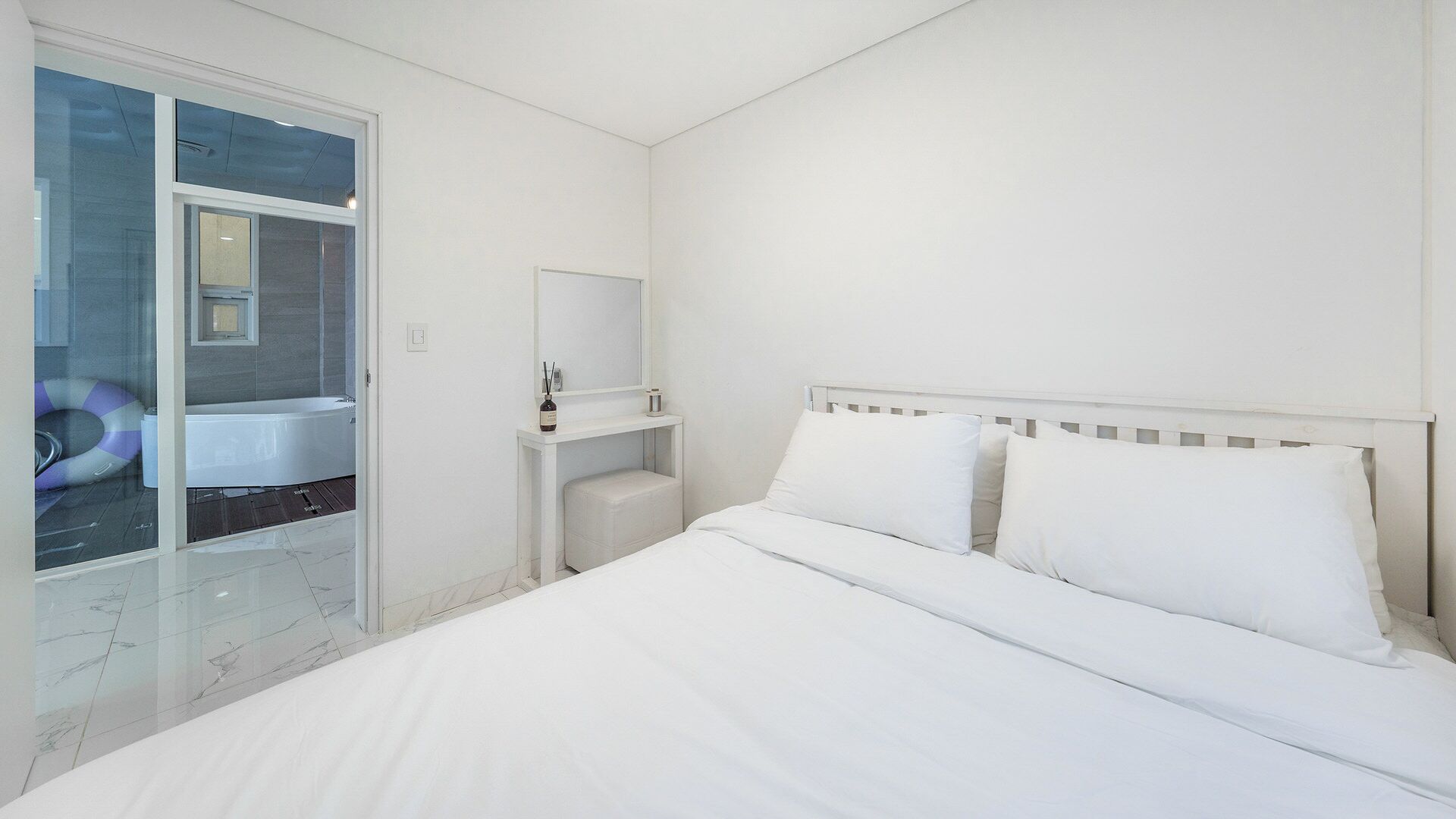 A hotel room with a bed, a nightstand, a mirror, and a view of a bathroom with a bathtub and a glass door.
