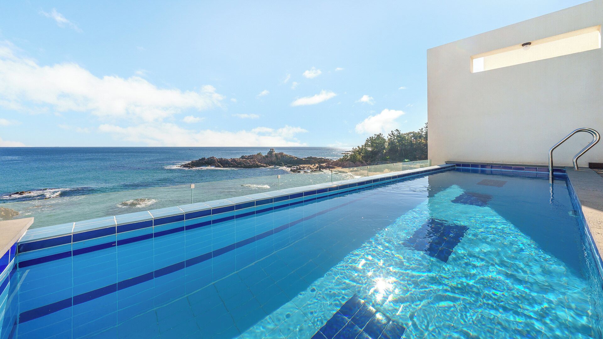 A clear blue pool with a view of the ocean and rocky outcrops.
