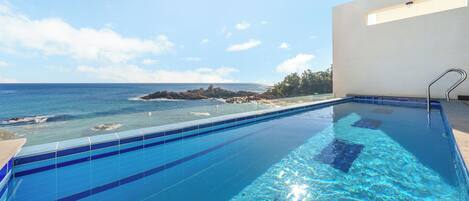 A clear blue pool with a view of the ocean and rocky outcrops.