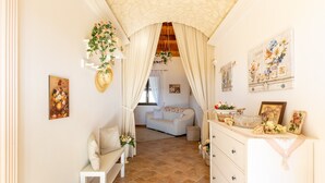 Una habitació amb un sofà blanc, un vetust blanc i una banca blanca. Hi ha decoracions florals i un quadre a la paret.