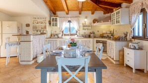 Una cuina amb bigues de fusta, taula de dinar, cadires i finestra amb cortines.