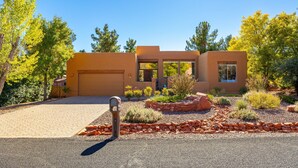 A modern two-story house with a garage, surrounded by a landscaped garden with various plants and a gravel driveway.