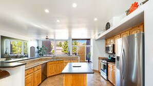 A modern kitchen with a central island, wooden cabinets, stainless steel appliances, and large windows offering views of the outdoors.